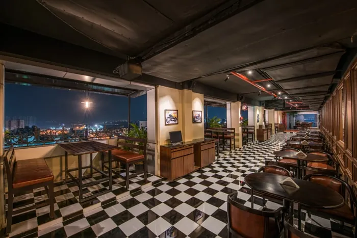 Indoor dining hall with a checkered floor and windows over the city