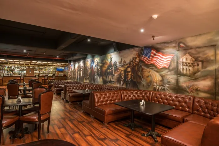 Leather booths below the painted mural in the indoor dining hall, with the bar behind